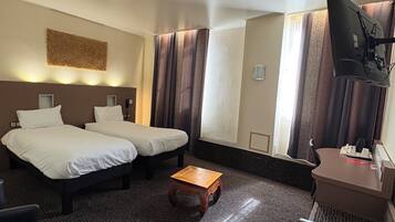 Habitación de hotel con dos camas, una pequeña mesa de madera, un escritorio con una silla, un televisor de pantalla plana y un elemento decorativo en la pared.