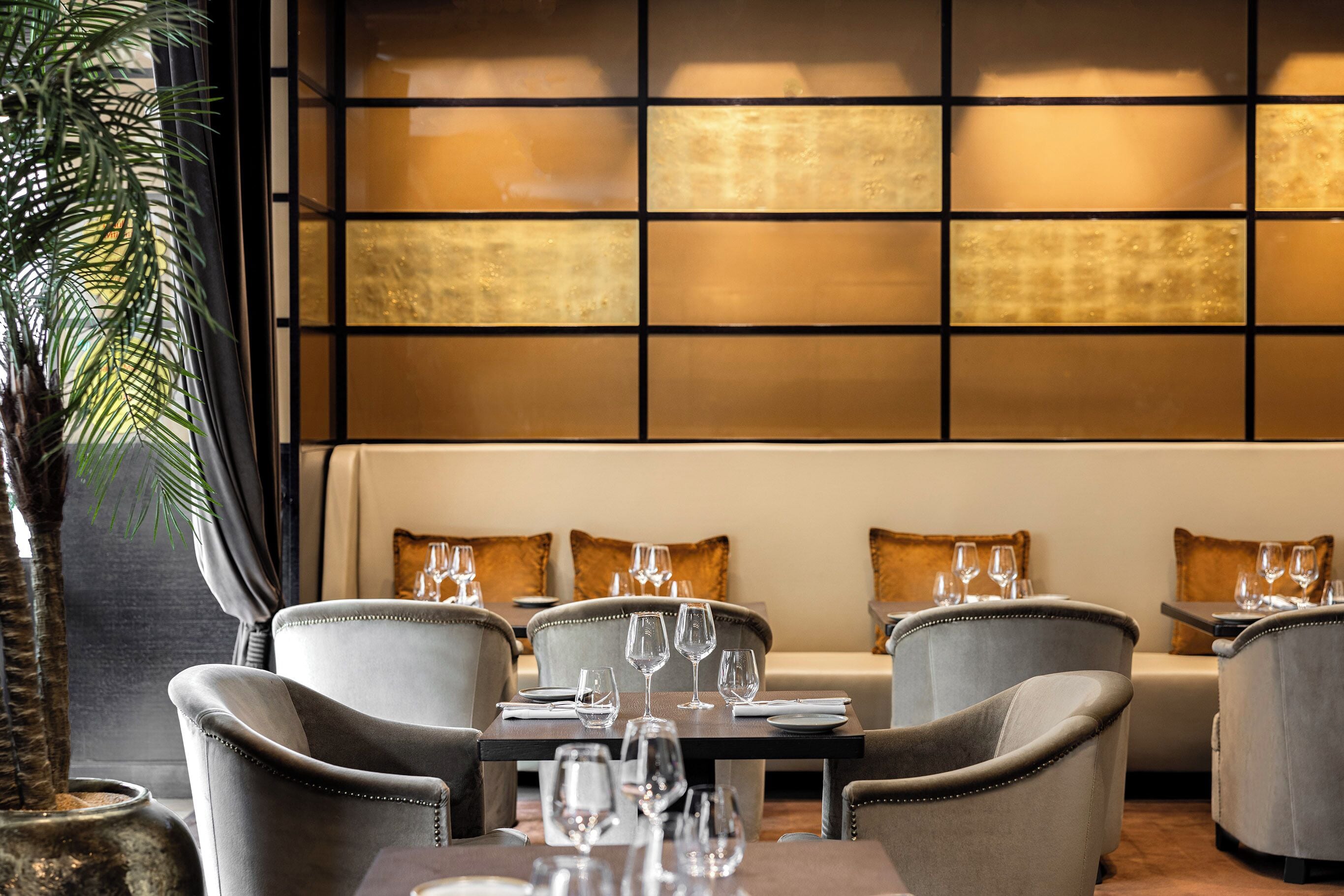 A restaurant with a modern interior, featuring a long table with multiple chairs, a sofa, and a decorative wall with a grid pattern.
