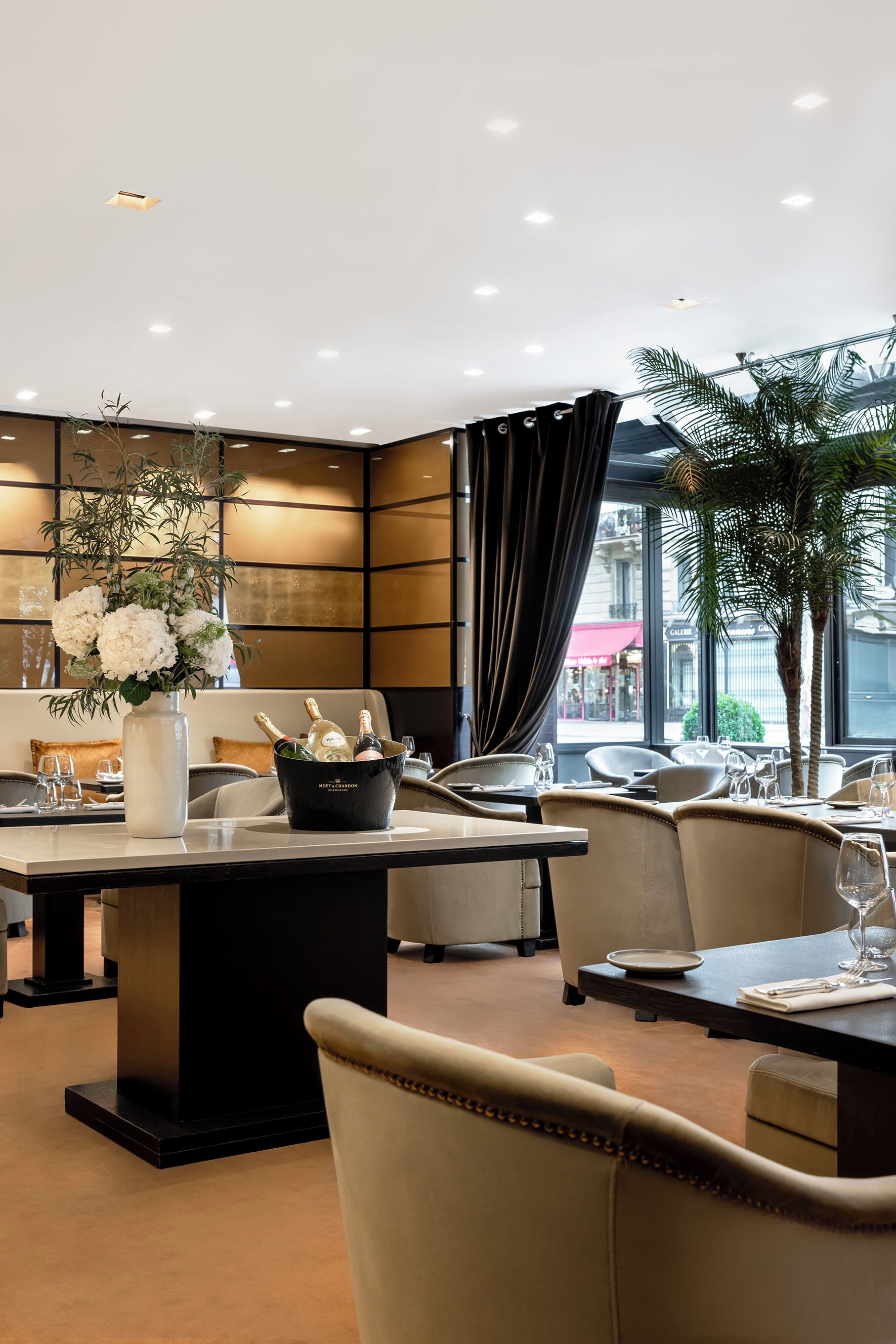 A modern dining area with a central table, chairs, a vase of flowers, and a bucket of champagne.
