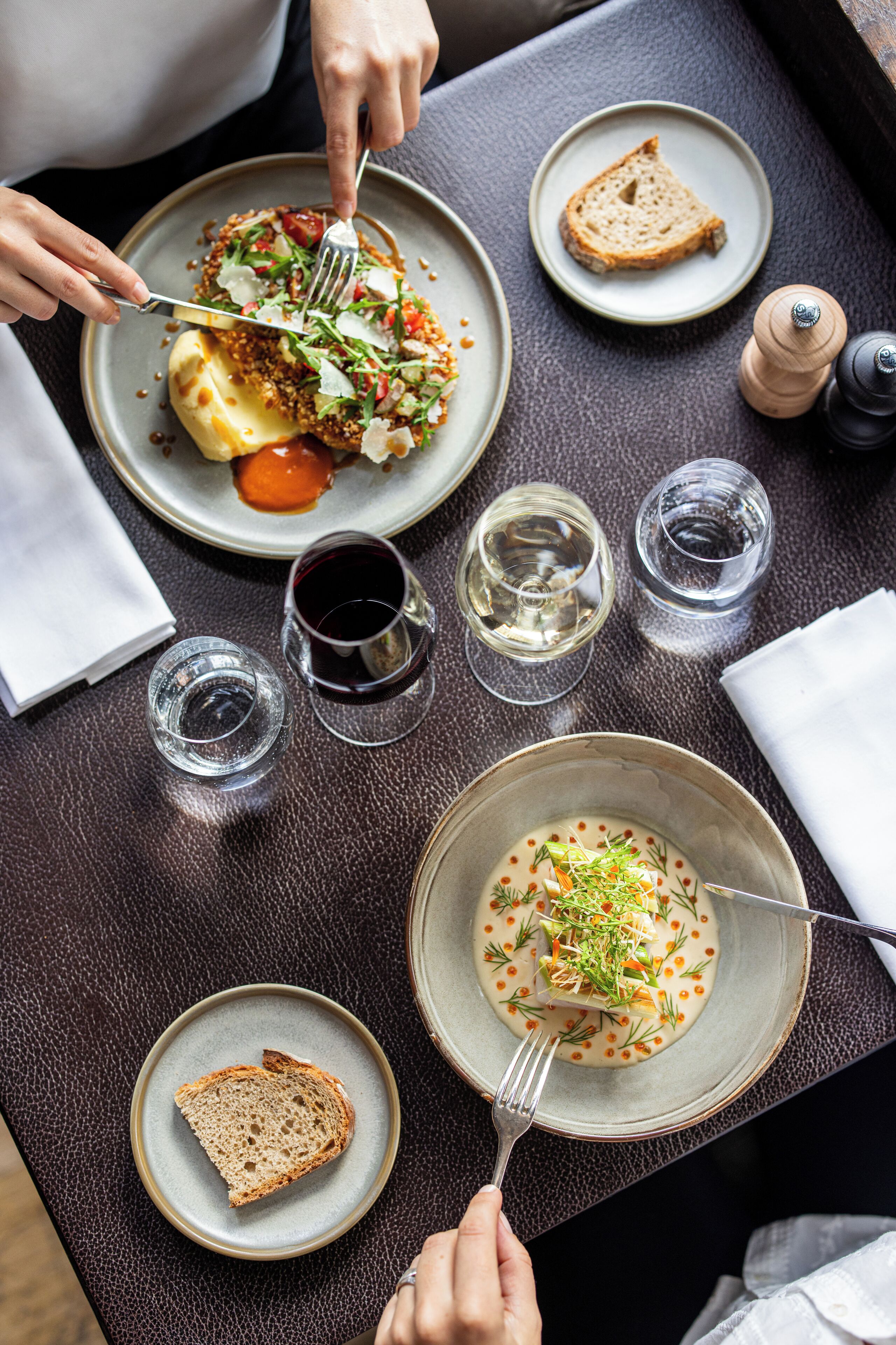 Een eettafel met borden eten, glazen wijn en een zout- en peperstel.
