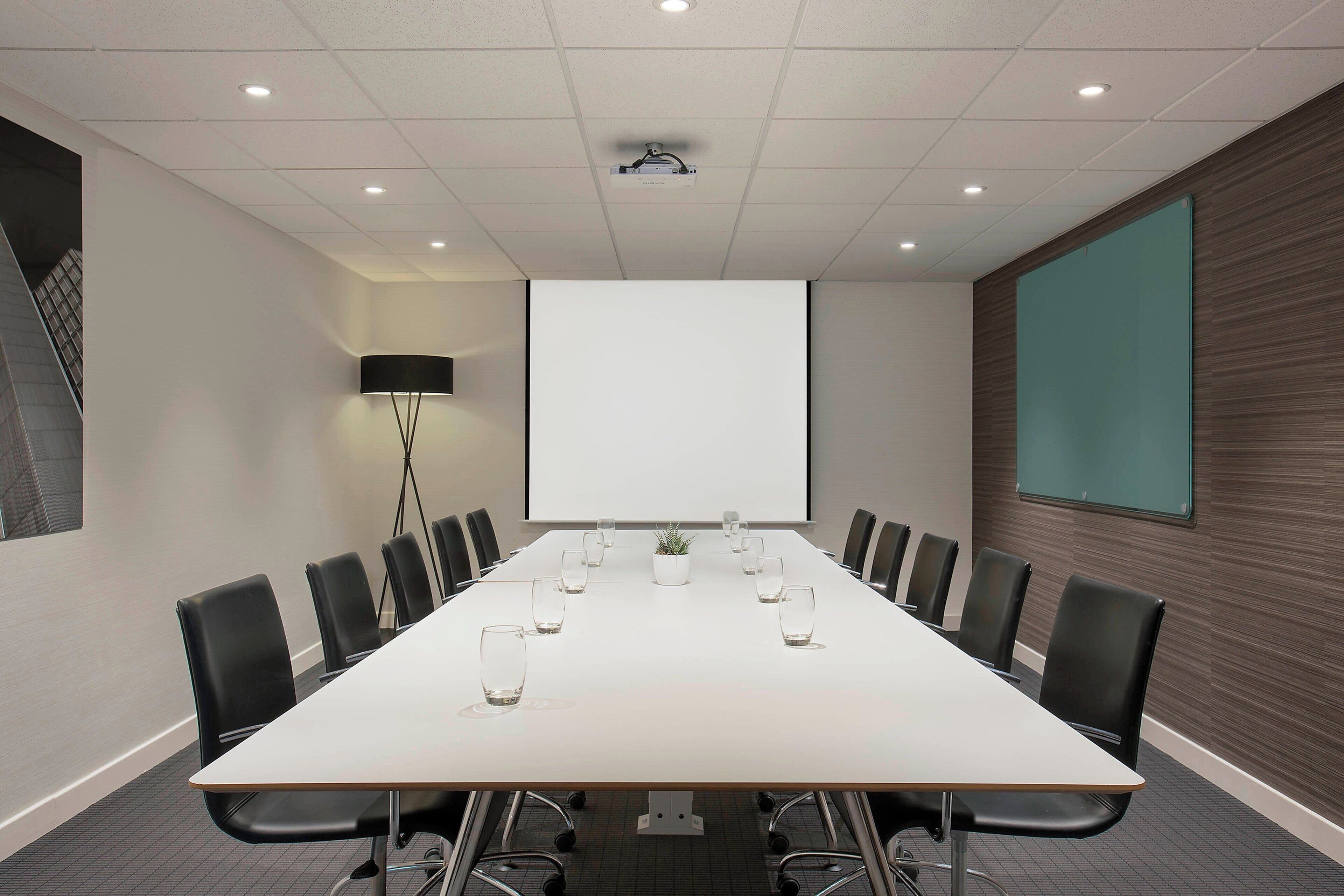 Una sala de conferencias con una larga mesa, sillas negras, una pantalla de proyector y una gran pantalla en la pared.