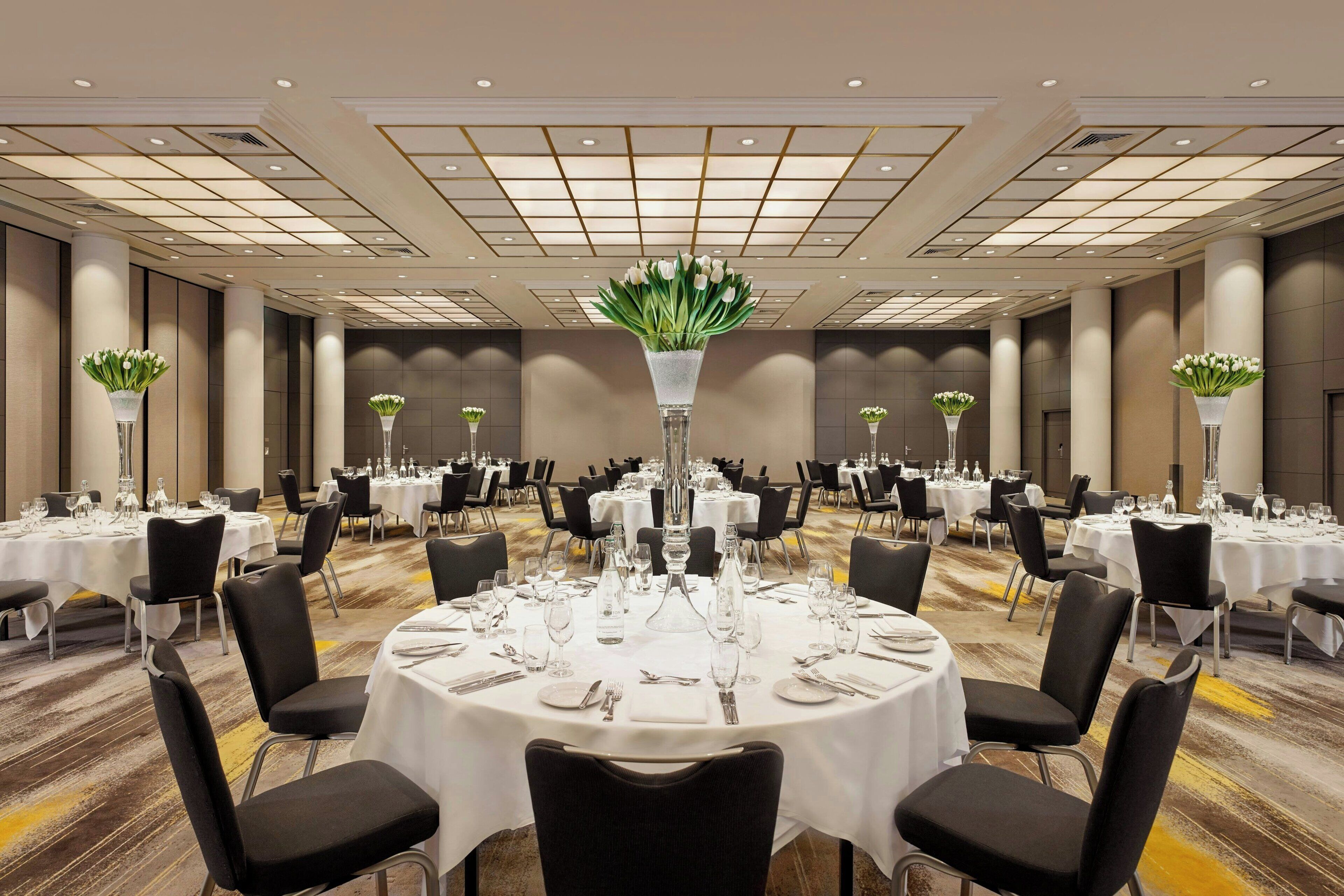 A banquet hall with round tables set for dining, each with chairs, white tablecloths, and centerpieces.
