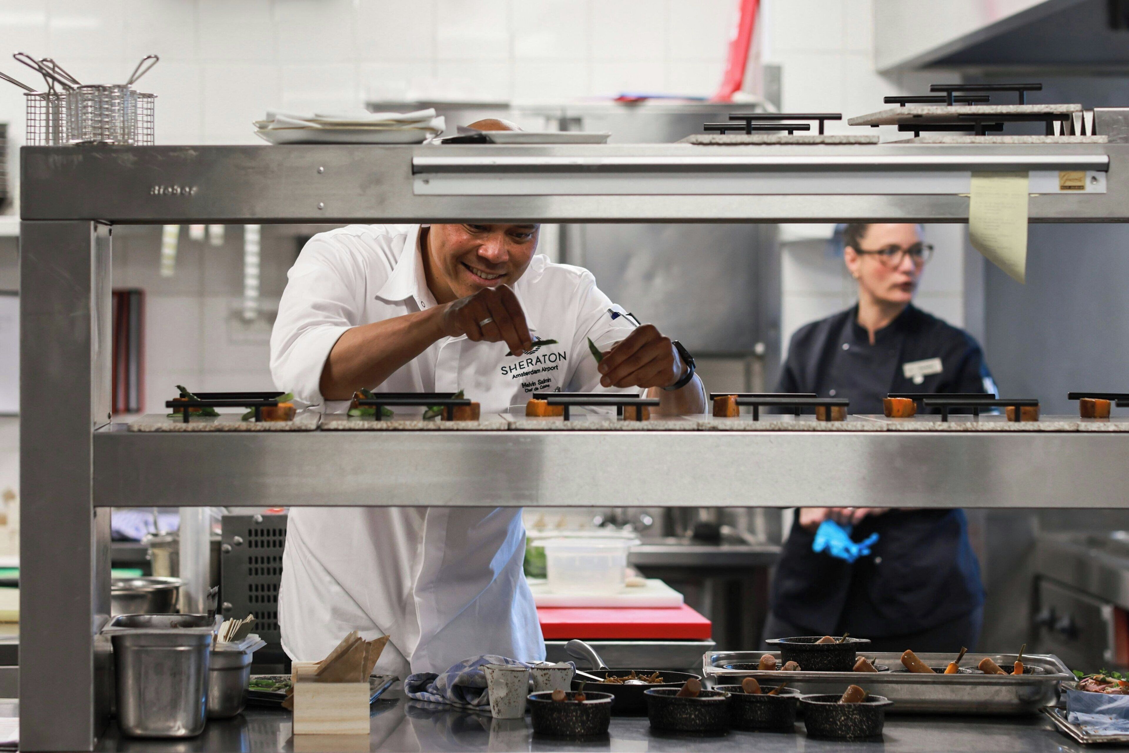 Un chef preparando comida en una cocina profesional con superficies de acero inoxidable y diversos utensilios de cocina.