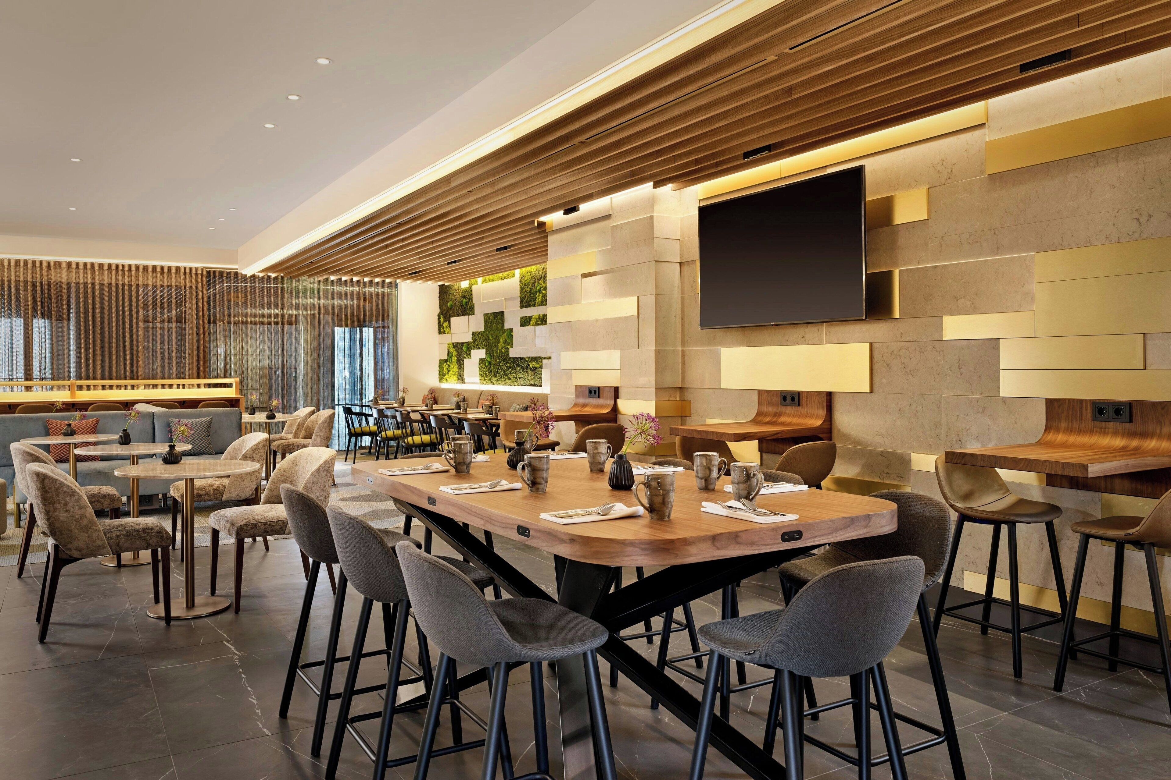 Un área de bar moderna con una mesa de madera larga, taburetes de bar y un televisor de pantalla plana montado en la pared.