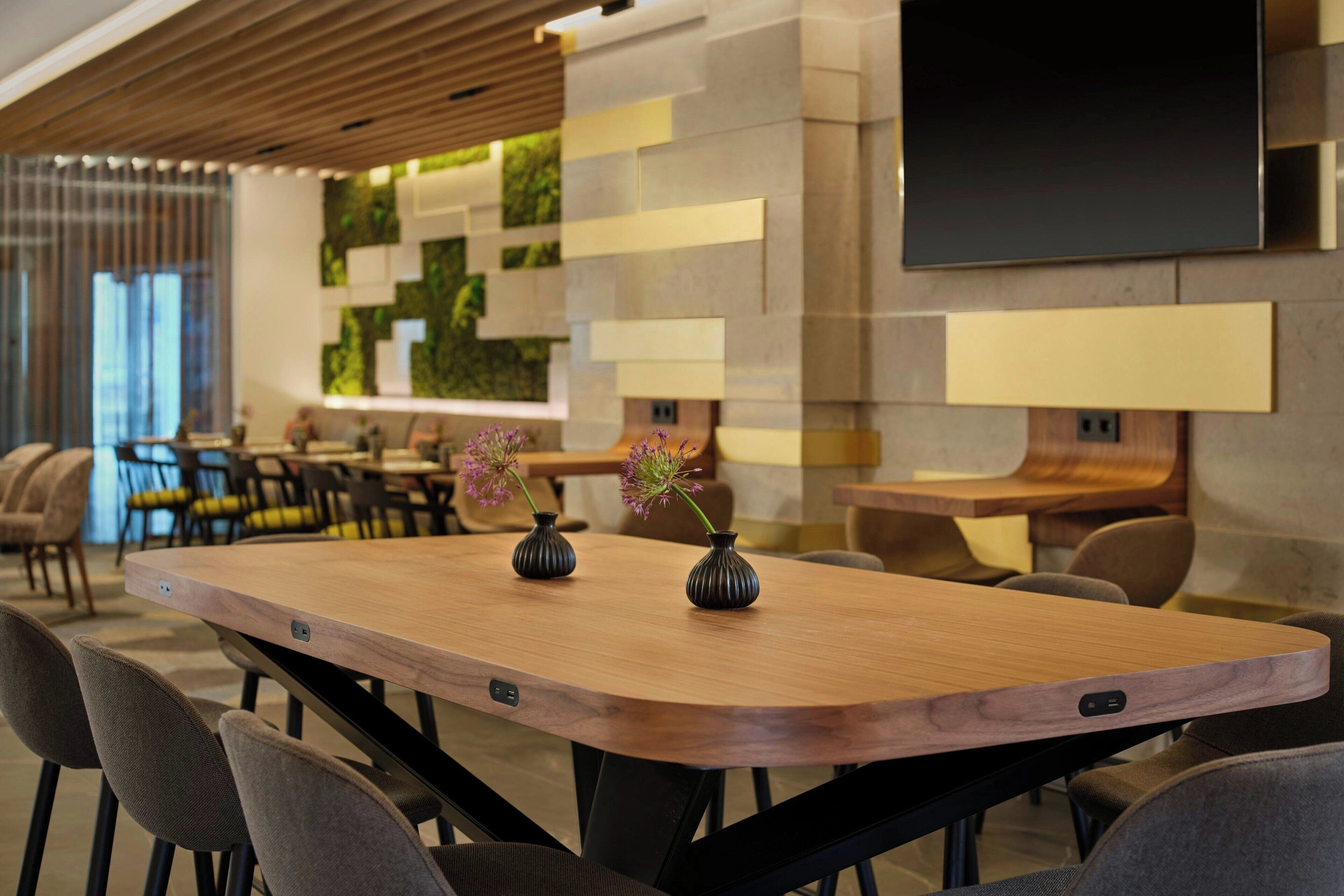 A modern conference room with a long wooden table, several chairs, and two vases with flowers.