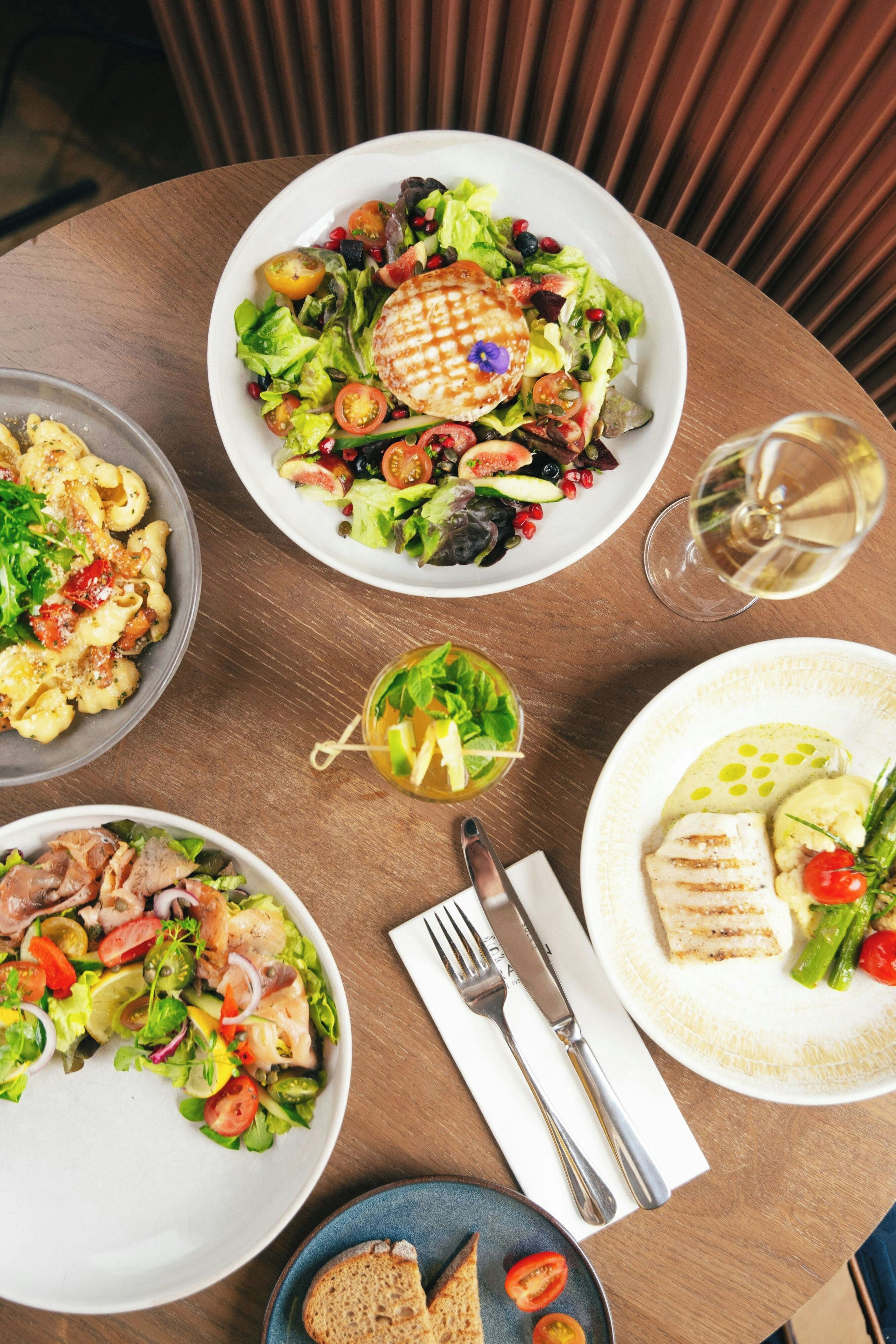 Une table de salle à manger ronde, avec différents plats, un verre à vin et des couverts.