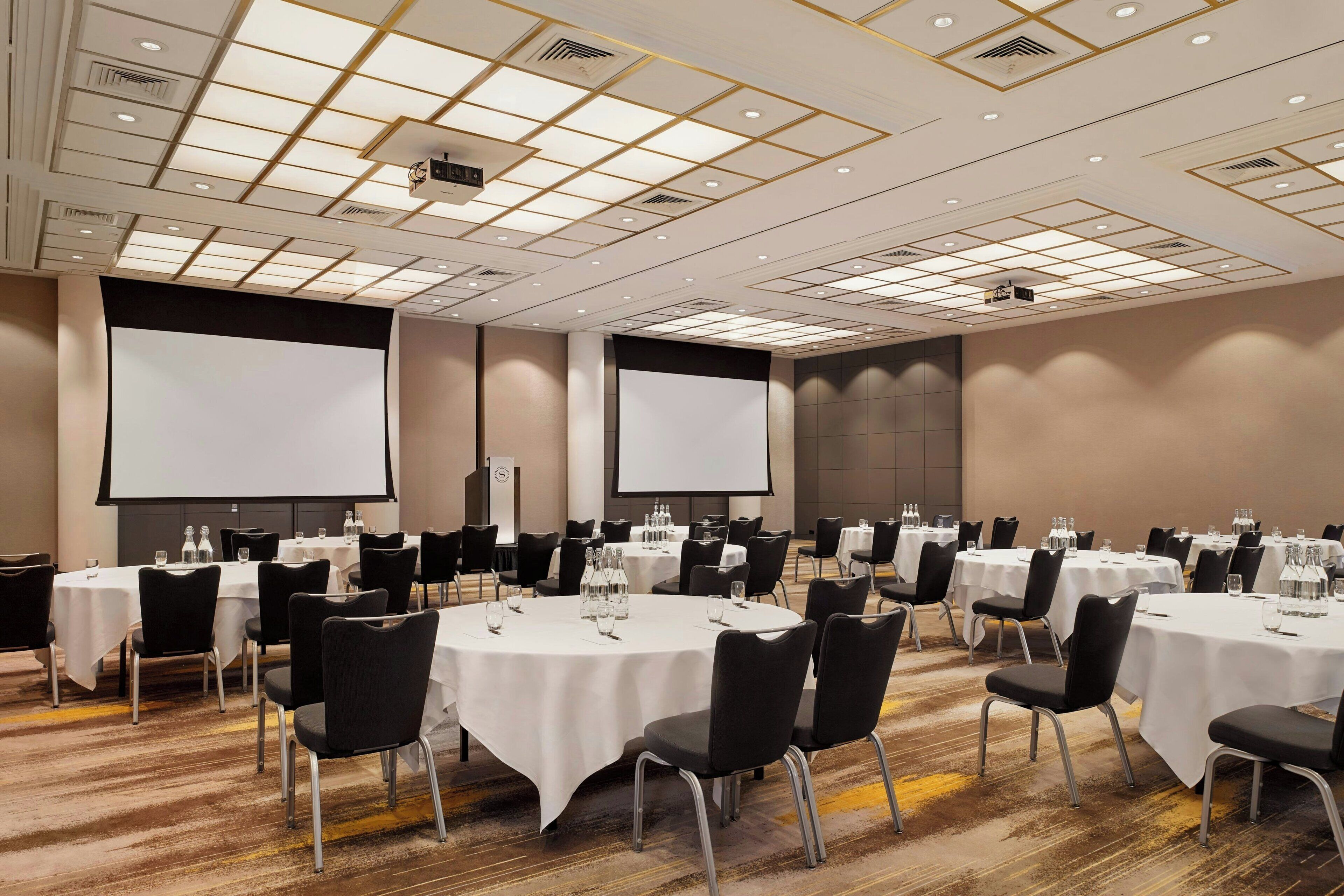 A conference room with multiple tables, chairs, and large screens.