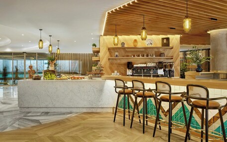 A modern bar area with a marble countertop, wooden bar stools, and pendant lighting.