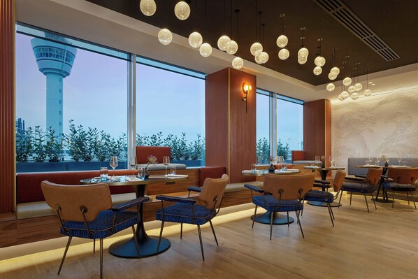 Un restaurante moderno con vistas a una torre, suelos de madera y mesas redondas con sillas azules.