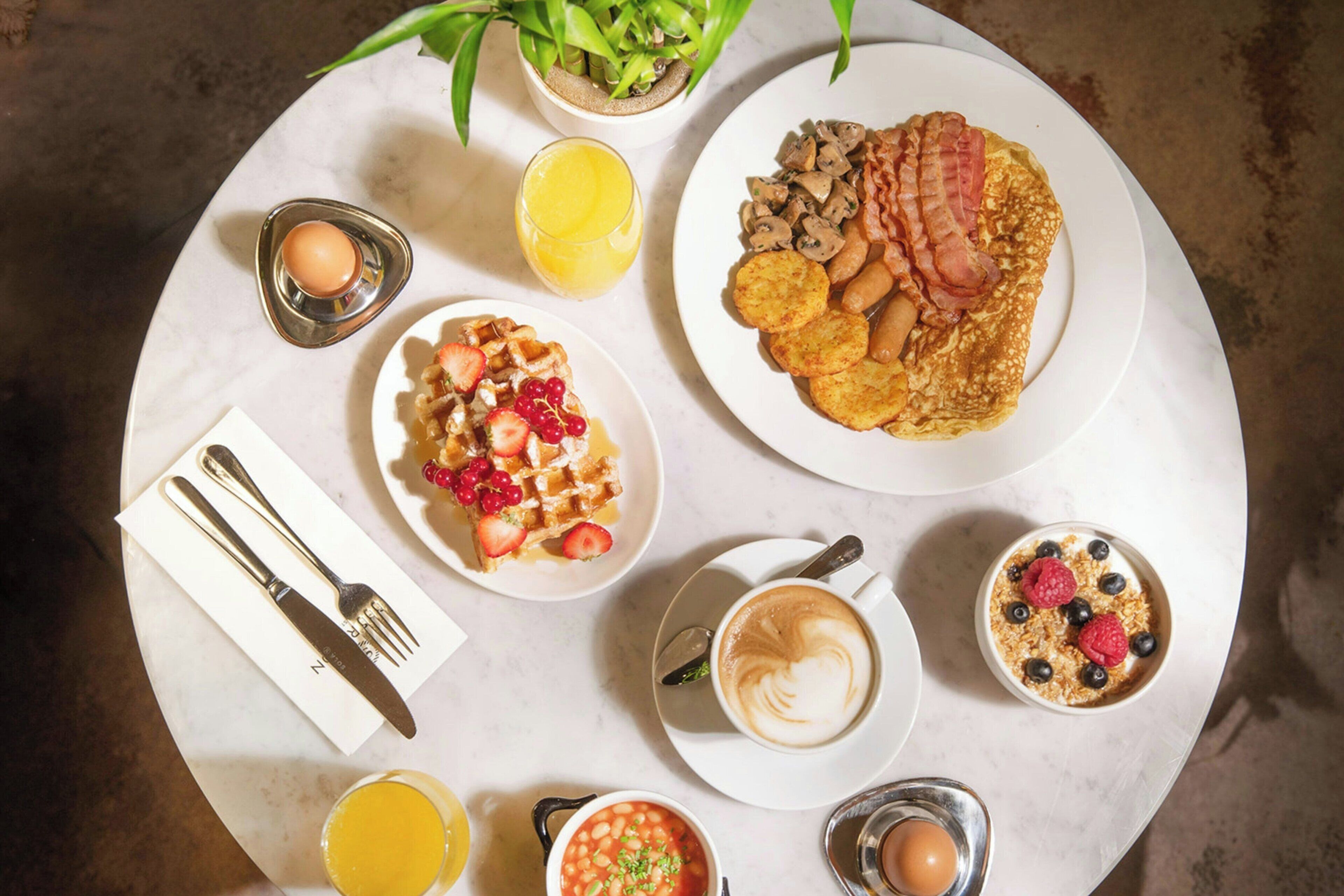 A breakfast setting with various dishes, a coffee cup, and a glass of orange juice on a round table.