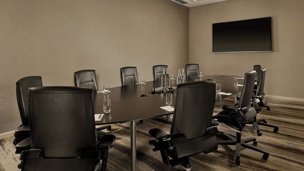 A conference room with a long table, black leather chairs, and a flat-screen TV on the wall.