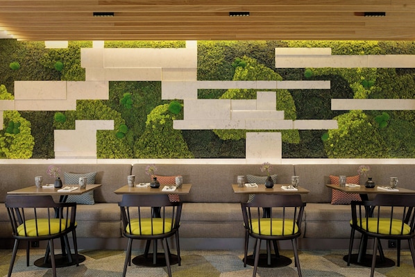 A restaurant with a green wall, cushioned seating, and tables with chairs.