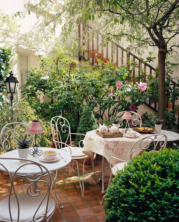 Un patio con una mesa redonda dispuesta para tomar té, rodeada de sillas y una pequeña planta en maceta.