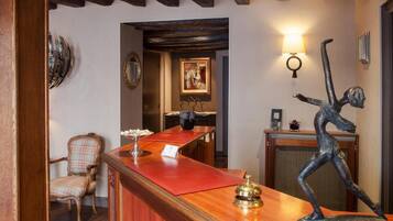 A reception area with a wooden reception desk, a chair, a statue, and a wall-mounted lamp.