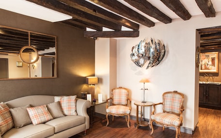 A room with a sofa, two armchairs, a round mirror, a lamp, and a wall-mounted abstract art piece.