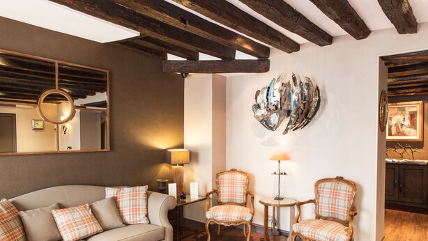 A room with a sofa, two armchairs, a round mirror, a lamp, and a wall-mounted abstract art piece. - Hotel la Residence du Berry (Versailles)