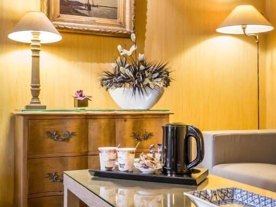 A room with a wooden wall, a framed picture, a glass table, two lamps, a sofa, and a coffee table with decorative items.