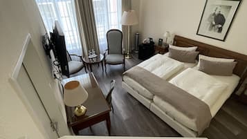 Habitación de hotel con una cama, un escritorio con lámpara, una silla, un televisor y una ventana con cortinas.