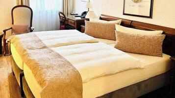 A double bed with a wooden frame, two bedside tables, a chair, a desk, and a framed portrait on the wall.