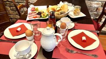 A breakfast setting with a variety of food items, including bread, fruits, and eggs, arranged on a table with red placemats and white plates.