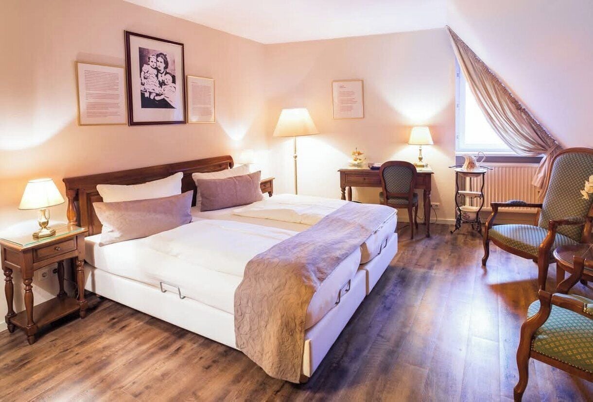 Habitación de hotel con una cama grande, mesitas de noche con lámparas, un escritorio, una silla y cuadros en la pared.