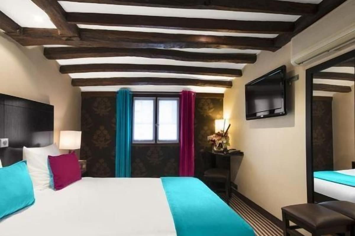 A hotel room with a bed, a desk, a chair, a TV, and a window with curtains.