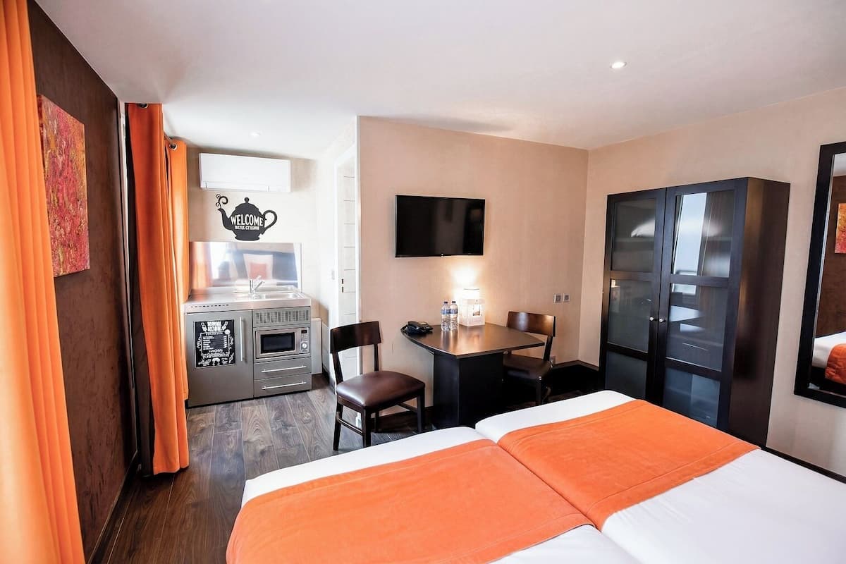 Habitación de hotel con cama, escritorio, silla, televisor, mini bar y armario.