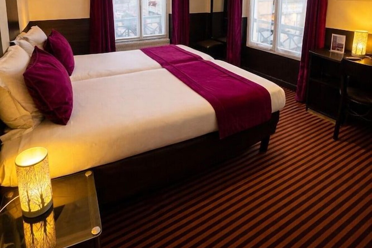 A hotel room with a large bed, a desk, a chair, a TV, and a window with curtains.