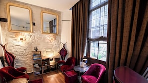 A room with a stone wall, two mirrors, a bookshelf, a table, and red chairs. - Hotel Pax Opera (Paris)