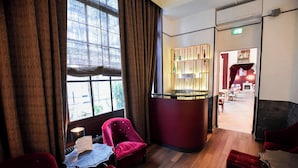 A hotel room with a large window, a red armchair, a small table, and a bar area with shelves. - Hotel Pax Opera (Paris)