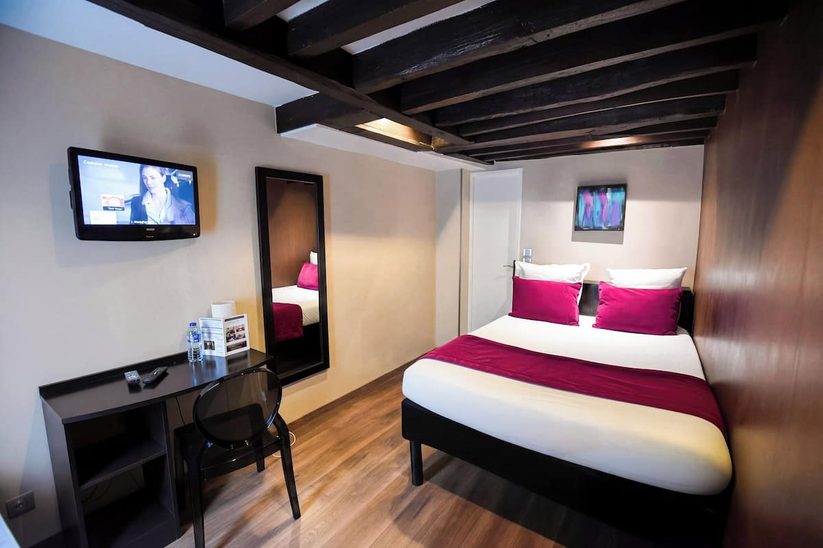 Una habitación de hotel con una cama, un escritorio, una silla, un televisor y un espejo.