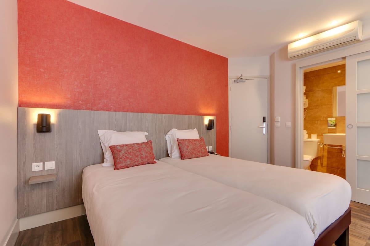 A double bed with two pillows, a wooden headboard, and a red accent wall.