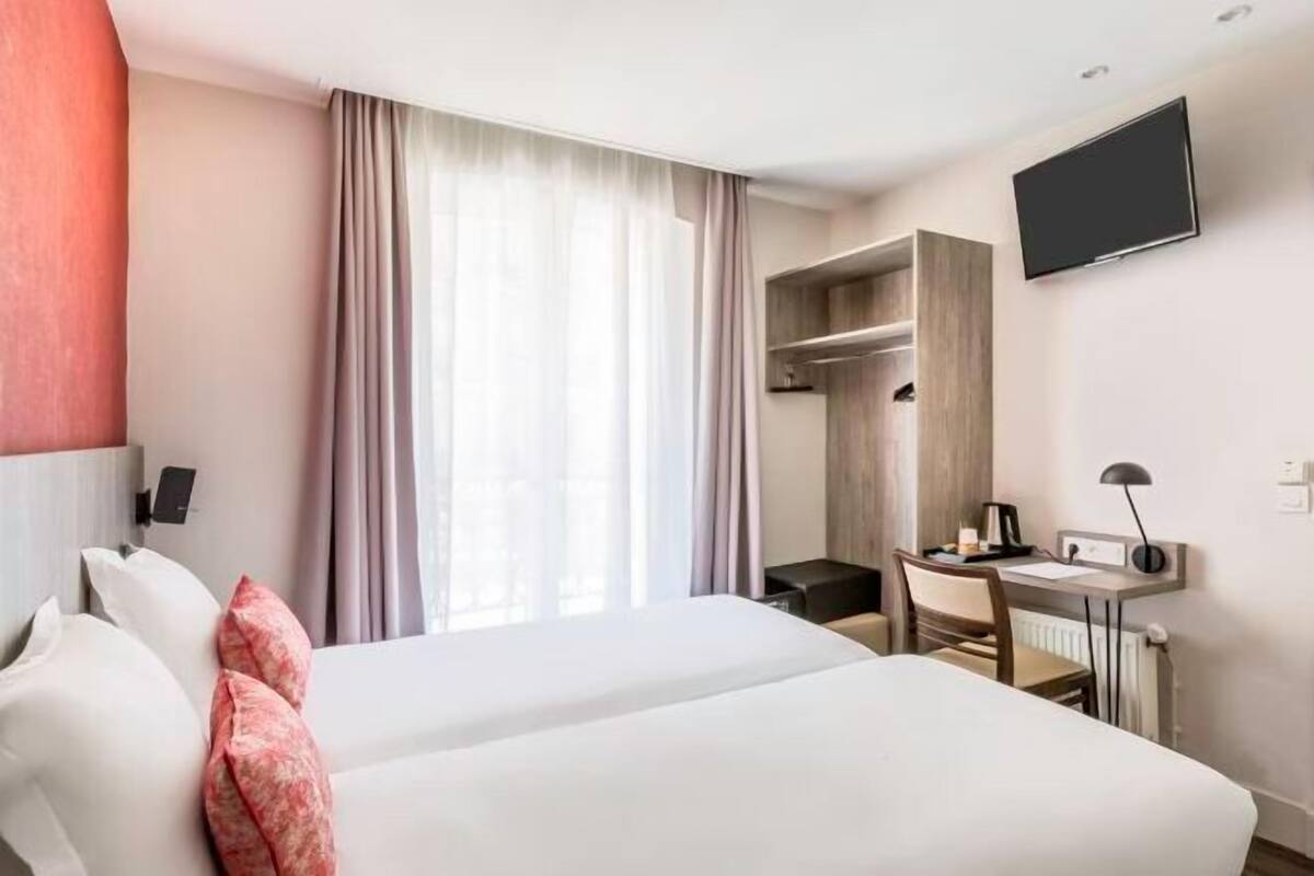 A hotel room with a bed, a desk, a chair, a TV, and a wardrobe.