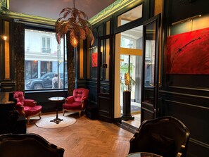 Un vestíbulo de hotel con un ventanal grande, un sillón rojo, una mesa redonda y una obra de arte moderno.