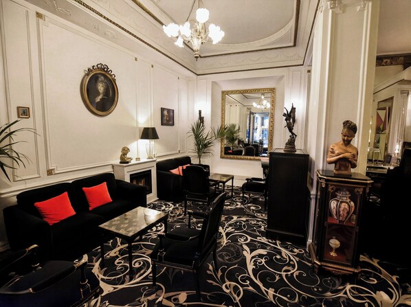 A formal room with a fireplace, a sofa with red cushions, a dining table with chairs, and a large mirror. - Hotel Peyris Opera (Paris)