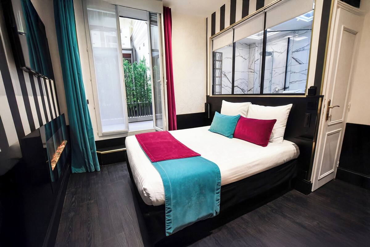 A bedroom with a bed, a window with a view, a door, and a curtain.