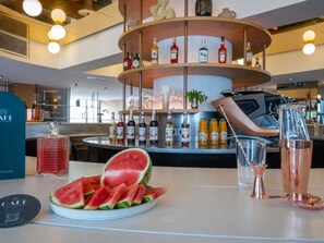 A bar area with a circular shelf of liquor bottles, a plate of watermelon slices, and a coffee machine.