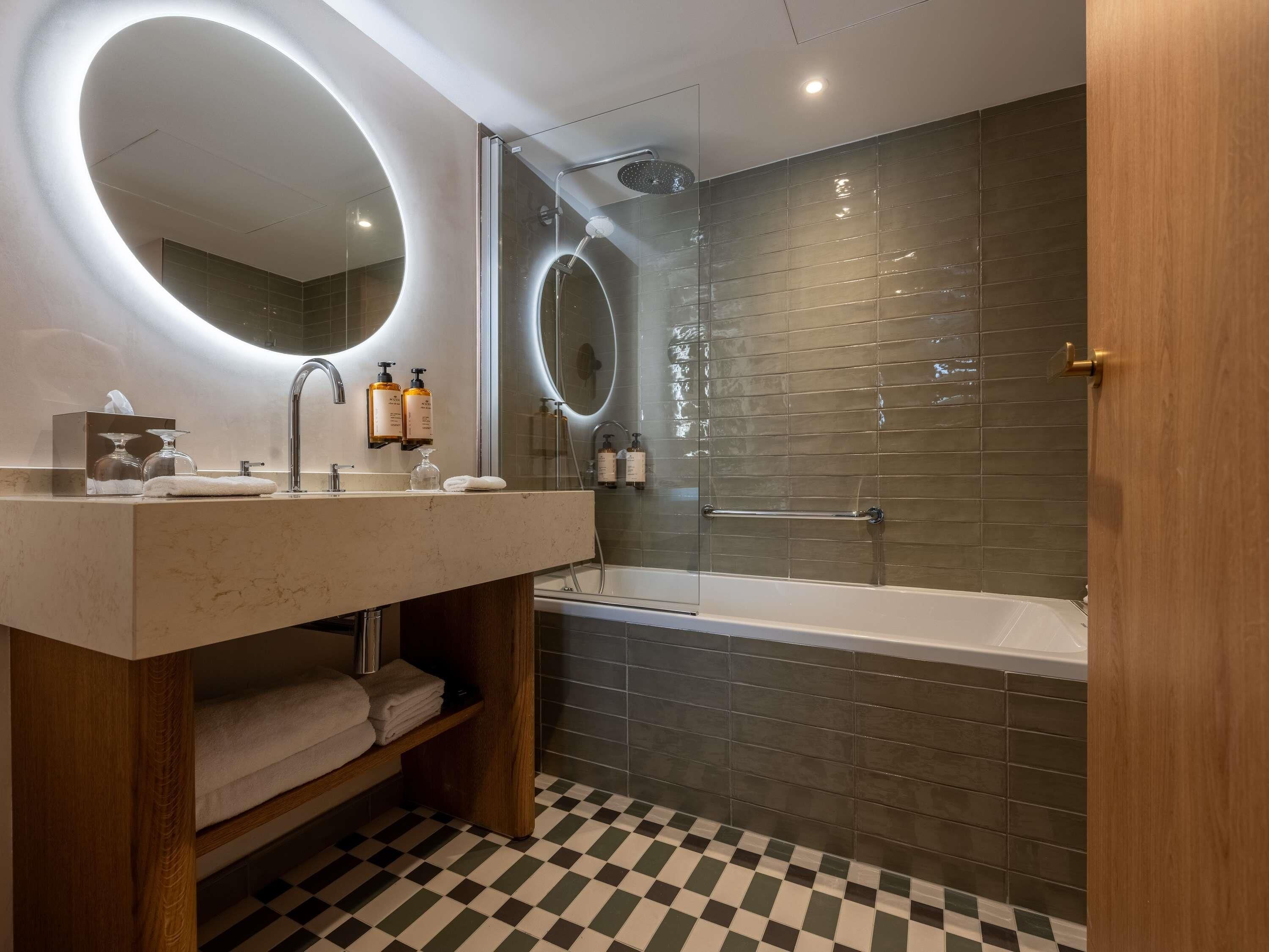 A modern bathroom with a large mirror, a bathtub, and a checkered floor.