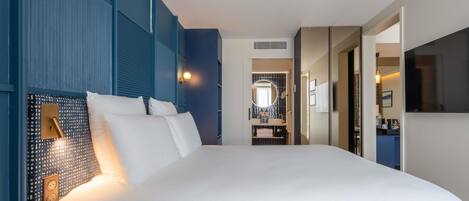Habitación de hotel con una cama grande, una lámpara de noche, un espejo y vistas al baño.