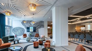 Un hall d’hôtel moderne doté d’un grand écran, d’espaces aménagés pour s’asseoir et d’une salle de conférence.