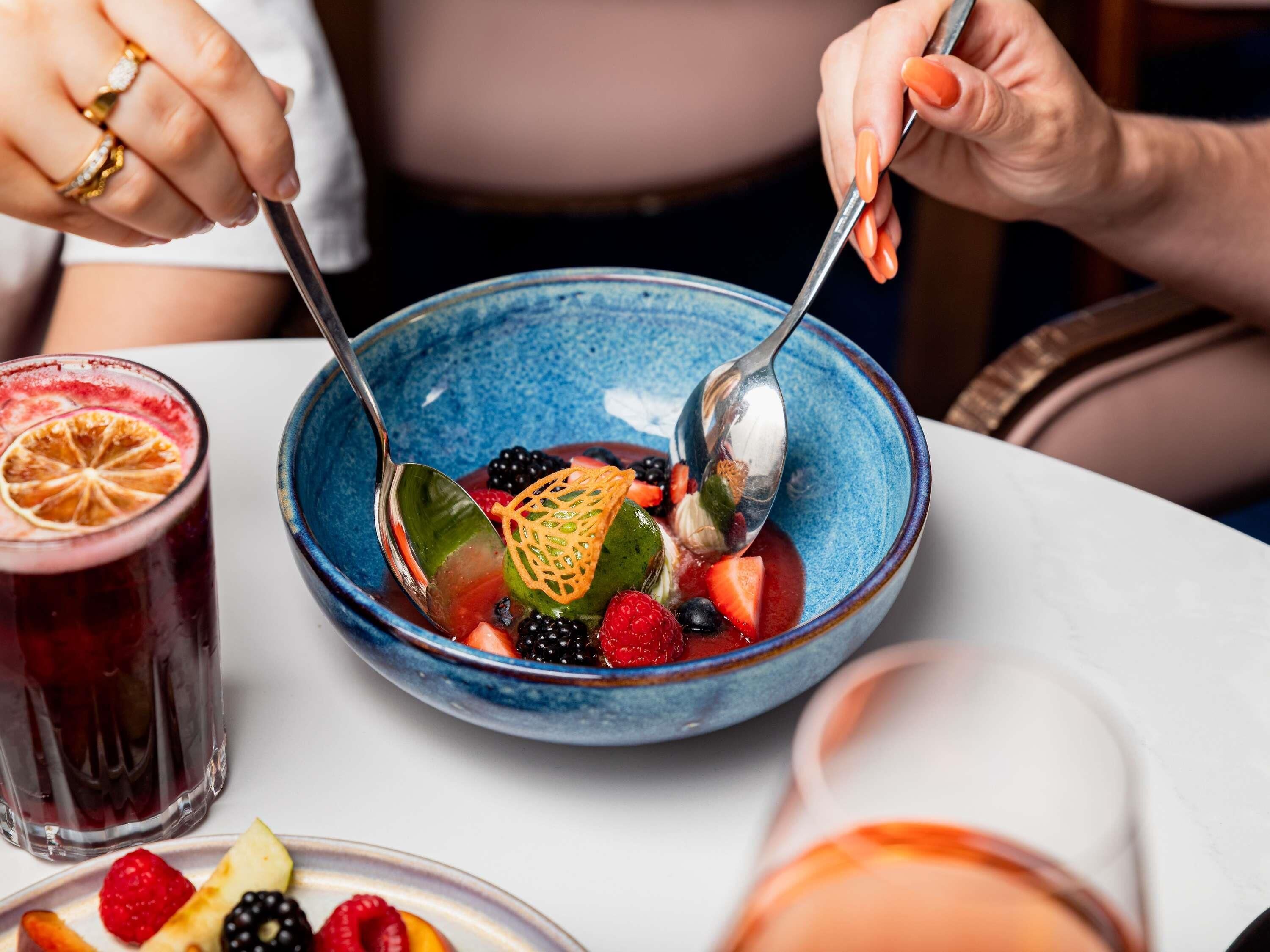 Iemand eet uit een blauwe kom met fruit en een lepel.
