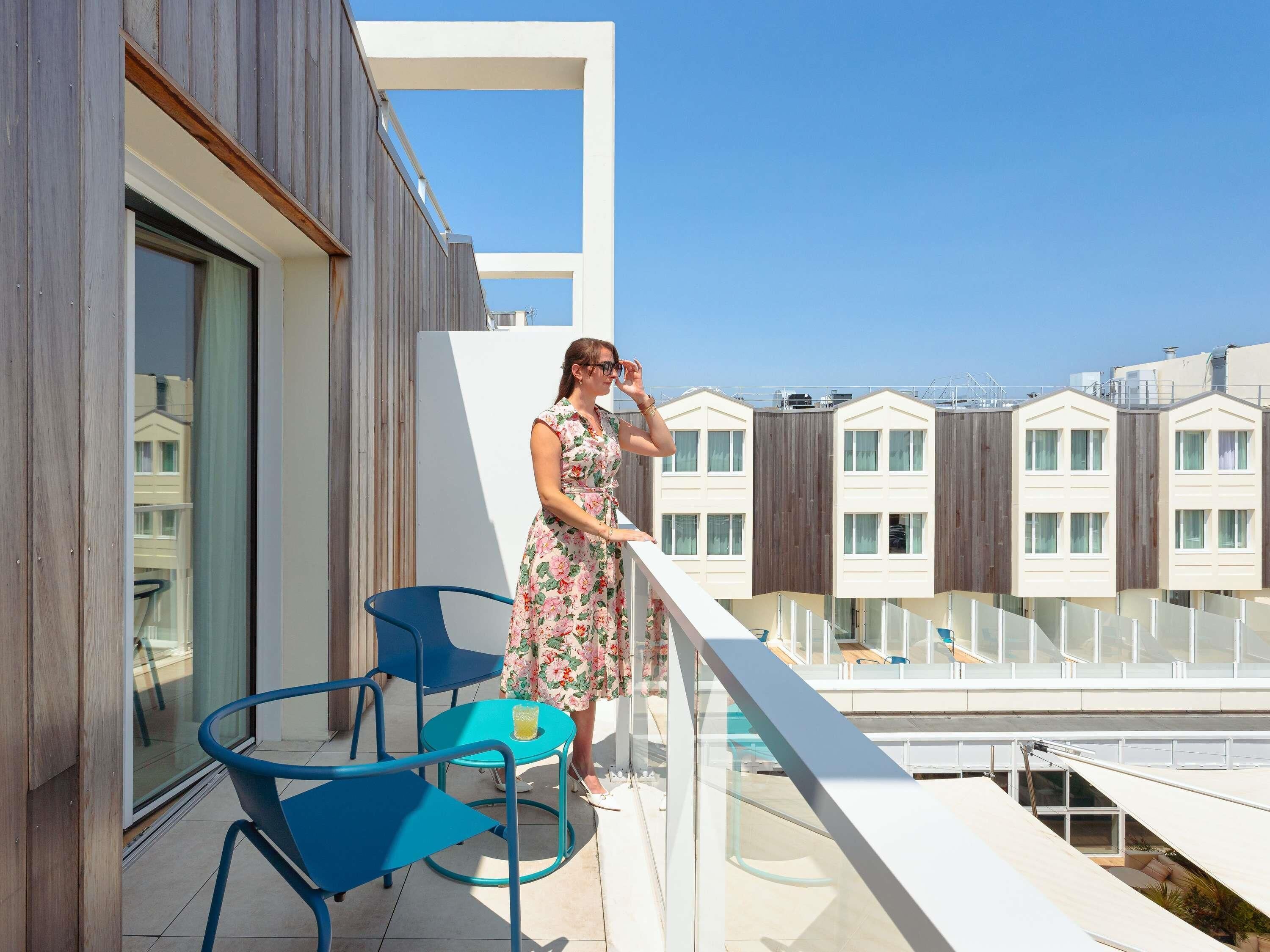 A balcony with a person, blue chairs, and a glass table.