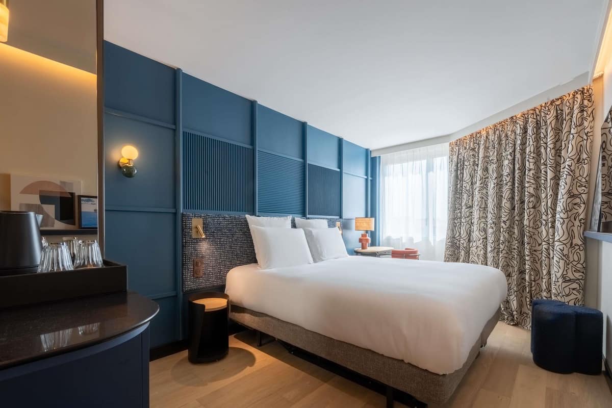 Une chambre d’hôtel moderne avec un grand lit, des tables de chevet, un bureau et une vue sur la mer.