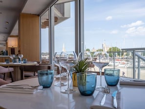 A dining table with wine glasses and a plant, overlooking a marina with boats and a tower. - Mercure La Rochelle Vieux-Port (La Rochelle)