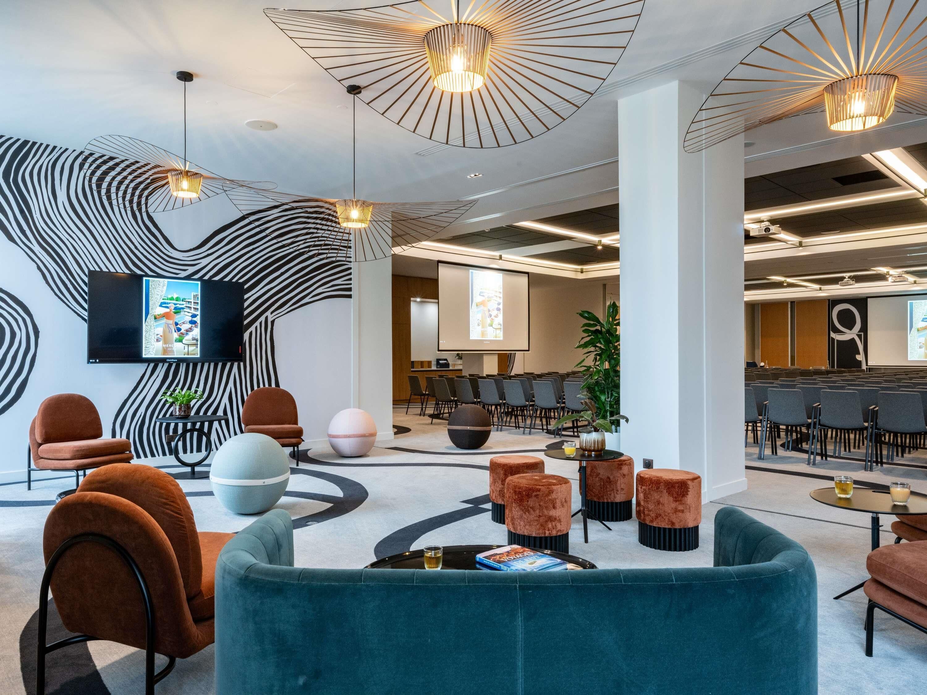 A modern conference room with a large screen, multiple seating arrangements, and contemporary lighting fixtures.