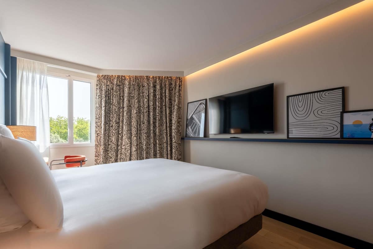 Una habitación de hotel moderna con una cama grande, un televisor de pantalla plana y obras de arte en la pared.