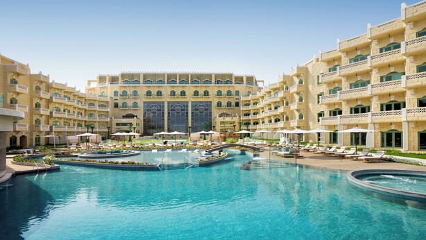 Un hotel con una amplia piscina central, varios balcones y un patio con sillones de descanso.