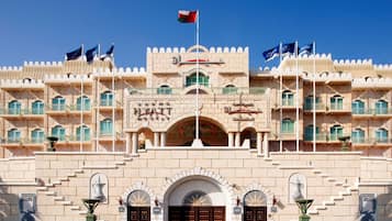 Experience the grand entrance of Grand Hyatt Muscat, featuring an impressive archway and balconies, surrounded by lush greenery and a tranquil fountain.