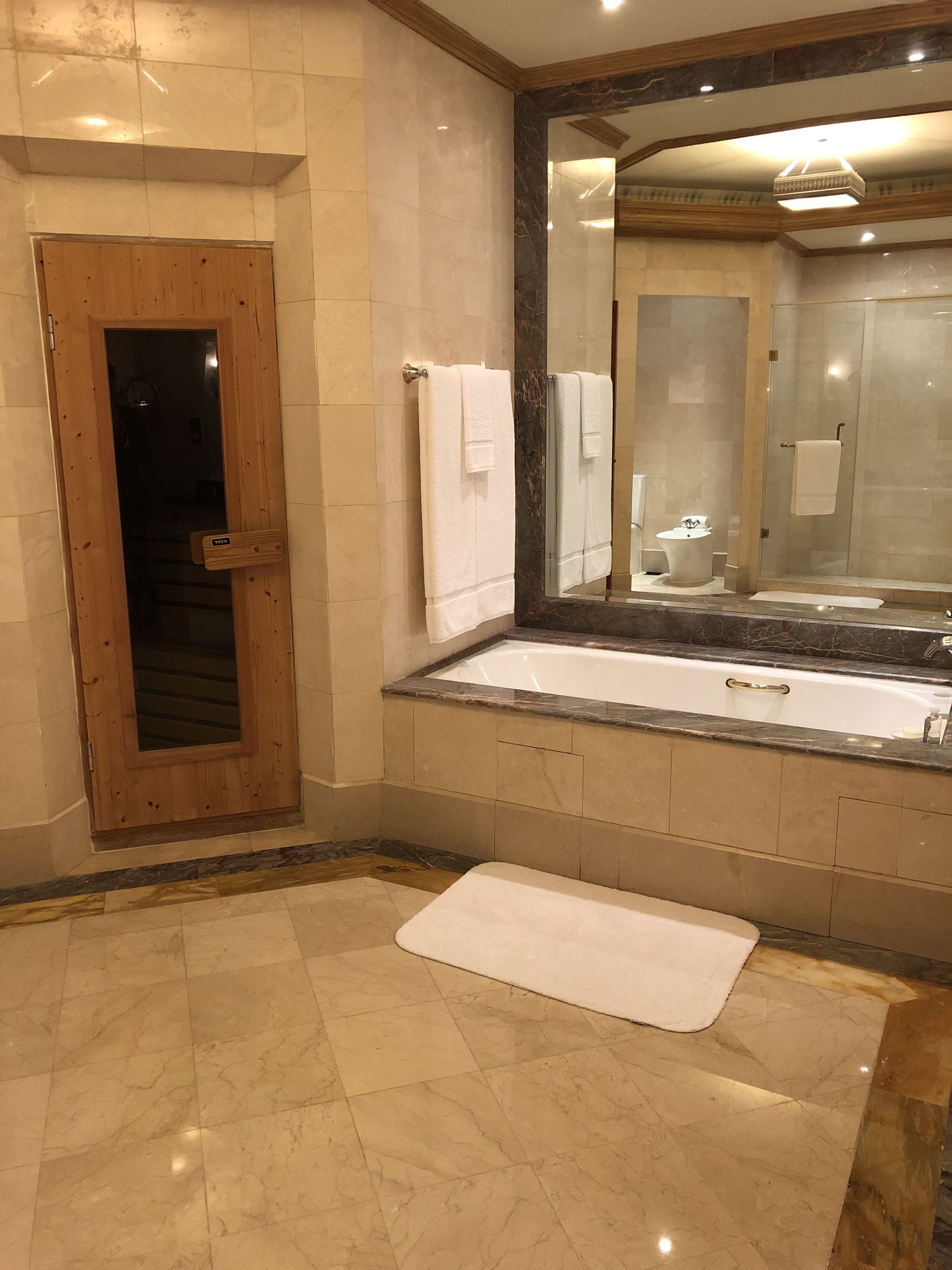 Ein Badezimmer mit Holztür, großem Spiegel, Badewanne und Waschbecken.