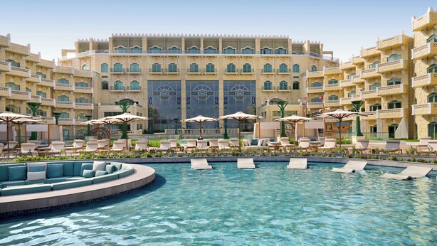 A hotel with a large pool, multiple lounge areas, and a grand building facade.